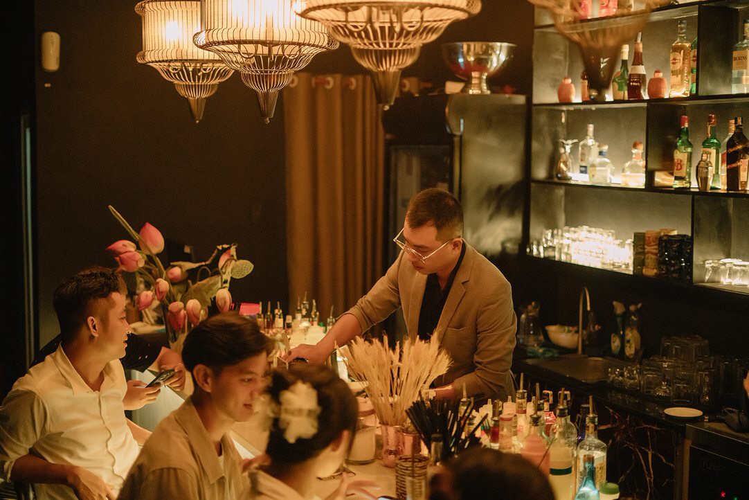 Người pha chế làm việc tại quầy bar dưới những chiếc đèn treo ấm màu