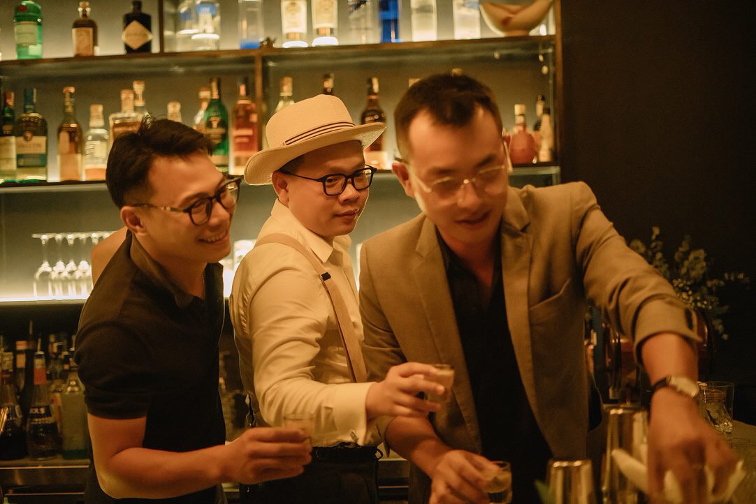 Ba người đứng sau quầy bar trong ánh đèn vàng ấm