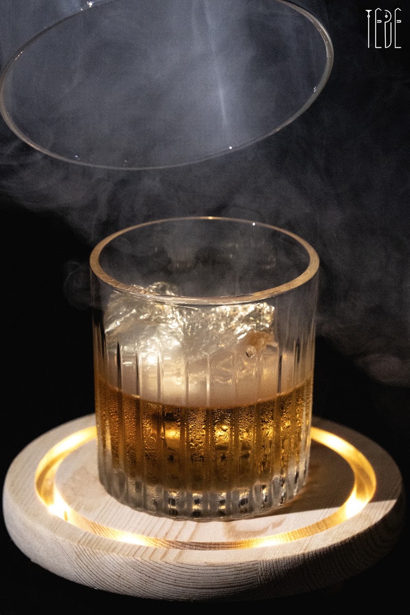 Ly cocktail màu hổ phách tỏa khói dưới nắp kính